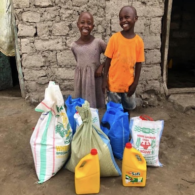 2 tanzanian children standing with bags of rices and other supplies